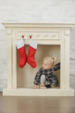 Evinde kırmızı Noel çoraplarıyla süslenmiş ahşap şöminenin önünde oynayan sevimli bir kız.