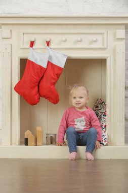Evinde kırmızı Noel çoraplarıyla süslenmiş ahşap şöminenin önünde oynayan sevimli bir kız.
