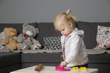 Yeni yürümeye başlayan kız kille oynuyor. Oyun hamuru çocukların iyi motor becerileri geliştirmesini, parmaklarını, ellerini ve bileklerini güçlendirmesini ve doğal olarak meraklı olmasını ve duyularını kullanarak dünyayı keşfetmesini sağlar.