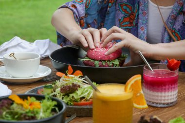 Vejetaryen pembe burger yiyen bir kadın. Restoran masasında servis edilen sağlıklı yemekler.