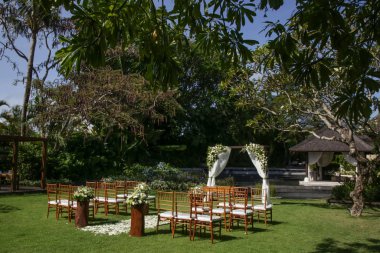 Tropik bahçede güzel romantik bir düğün, ahşap sandalyeler ve beyaz çiçeklerle süslenmiş basit bir çardak.