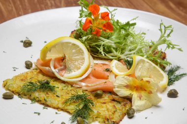 Patates kızartmalı füme somon, yeşil salata ve limon dilimleriyle süslenmiş. Enfes bir yemek. Yaratıcı restoran yemeği konsepti.