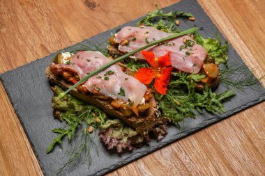 Açık yüzlü sandviç, jambonlu kızarmış tahıl ekmeği, peynir, otlar ve yeşil yaprak salatası.