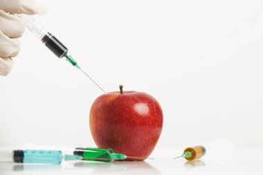 Kırmızı elmaya enjekte edilen iğnenin yakın çekimi, genetik mühendislik ürünü gıda konsepti.