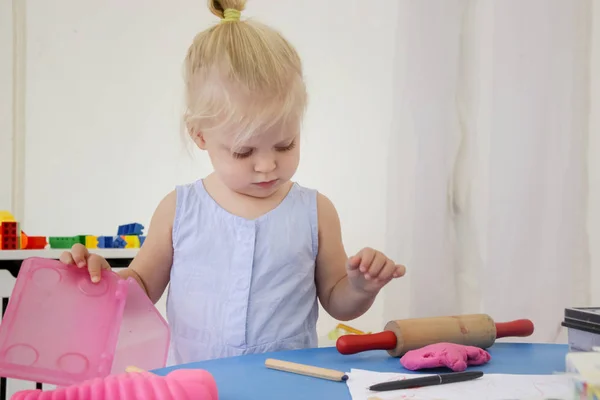 Toddler girl playing with modelling clay. Play dough allows kids to develop fine motor skills, strengthen fingers, hands and wrists and to be naturally curious and explore the world using their senses