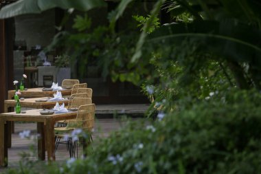 Lüks restoranda ya da cafe terasında yeşil ve çiçekli ahşap masalar ve sandalyeler.