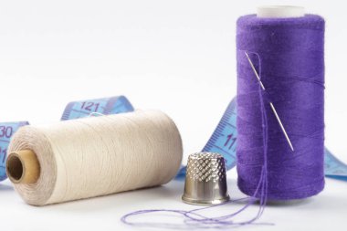 İğneli mor iplik makarası, beyaza farklı dikiş malzemeleri.