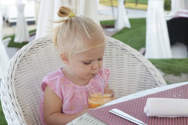 レストランのテーブルに座って 新鮮な絞りオレンジジュースを飲んで幸せな幼児の女の子 — ストック写真
