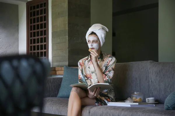 Jovem Mulher Sentada Casa Com Máscara Beleza Facial Enquanto Livro — Fotografia de Stock