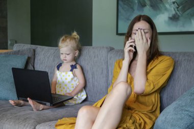 Anne ve kızı oturma odasında kanepede oturup dizüstü bilgisayar ve cep telefonuyla vakit geçiriyorlar. Modern aile yaşamı, teknoloji ve internet bağımlılığı kavramı.
