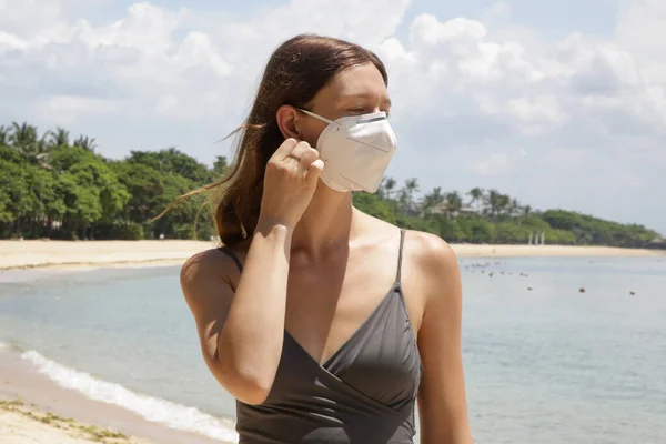 Woman with disposable surgical mask alone on the beach. Empty beach during coronavirus lockdown. Coronavirus pandemic crisis. Tourism is entering a great crisis due to the worldwide panic of the Corona Virus.