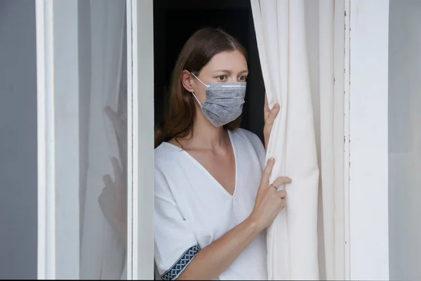 Jeune Femme Avec Masque Chirurgical Jetable Regardant Par Fenêtre Ennuyé — Photo