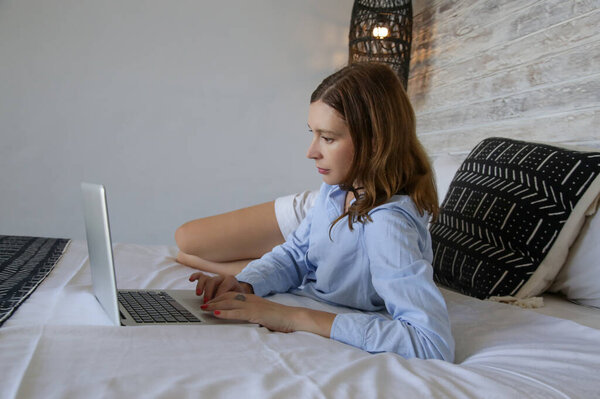 Молодая красивая женщина работает на ноутбуке в постели
 