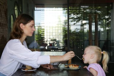 Anne kızını çikolatalı pastayla besliyor. Çikolatalı pasta yiyen küçük bir kızın samimi portresi. Mutlu çocukluk kavramı.