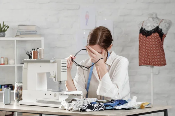 Sleepy, frustrated, exhausted seamstress with headache on her work desk. Small business or self-employed problems. Deadline or overwork concept, bored or getting tired at work in creative industry.