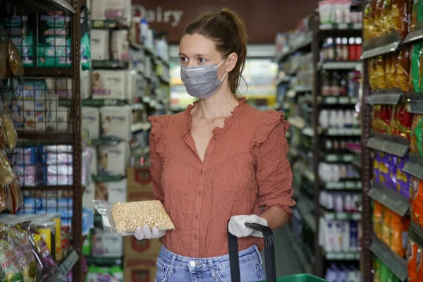 Woman wearing protective mask while grocery shopping in supermarket, Coronavirus contagion fears concept