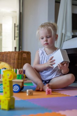 Sevimli küçük kız yerde tek başına oynuyor. Oyuncaklarla oynayan iki yaşındaki bir çocuğun samimi portresi..