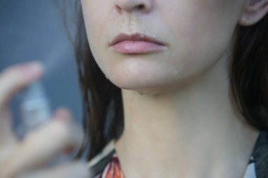 Yüzüne sprey sıkan bir kadın, yaz mevsimi cilt bakımı konsepti.