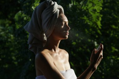 Yüzüne sprey sıkan bir kadın, yaz mevsimi cilt bakımı konsepti.