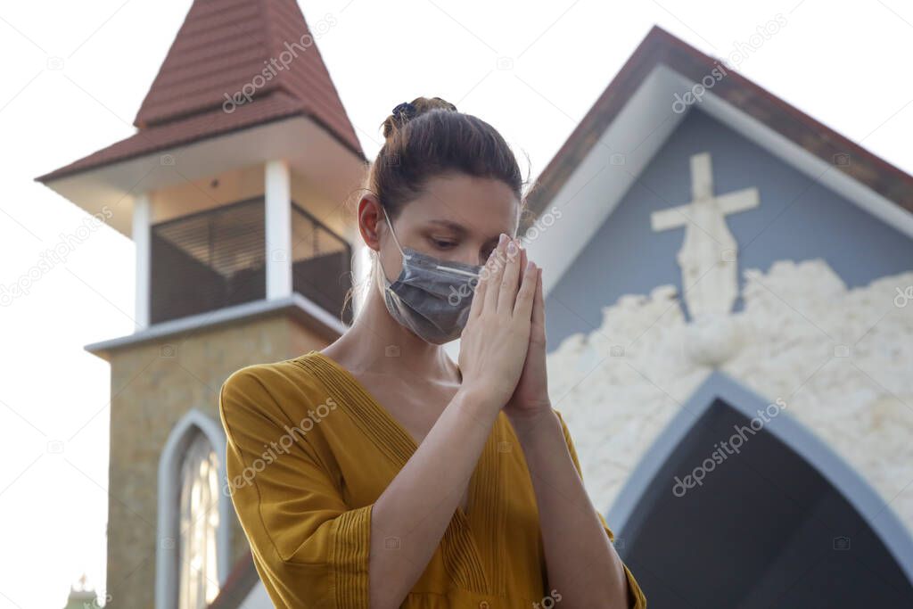 Woman wearing protective medical mask in front of church. Religious hope concept in challenging times. Corona virus outbreak and air pollution concept.