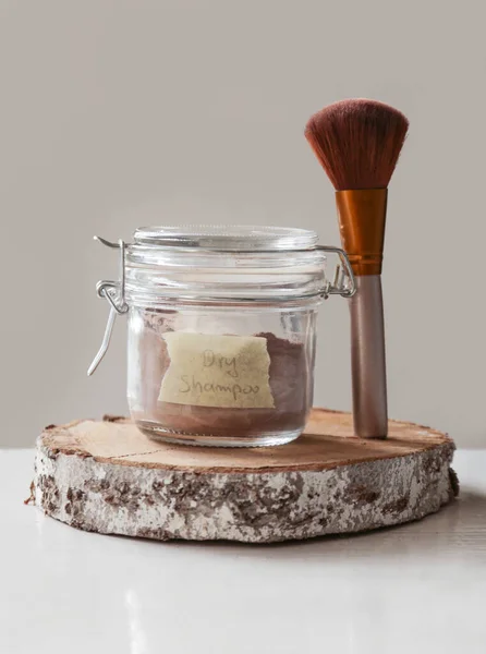 A jar of organic non-toxic chemicals free dry shampoo. DIY project for healthy low toxic living. Simple shampoo powder containing just natural ingredients, cocoa powder, cornstarch and essential oil.