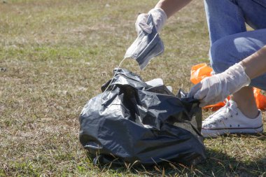 Çayırdan kullanılmış tıbbi maskeler alan bir kadın. Koronavirüs maskesi toplayan çevreci aktivistin fotoğrafı..
