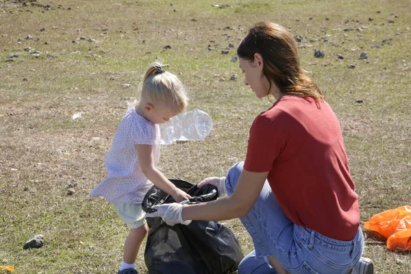 幼児の女の子と草原からプラスチックごみを拾う若い女性 ゴミの収集は 子どもたちが環境保護に関わる教育活動です — ストック写真