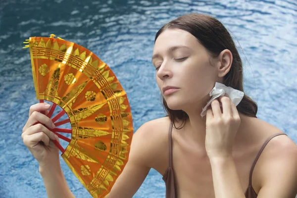 ファンで熱波と戦う女性 暑い夏の日に水の横にいる若い女性の肖像画 — ストック写真