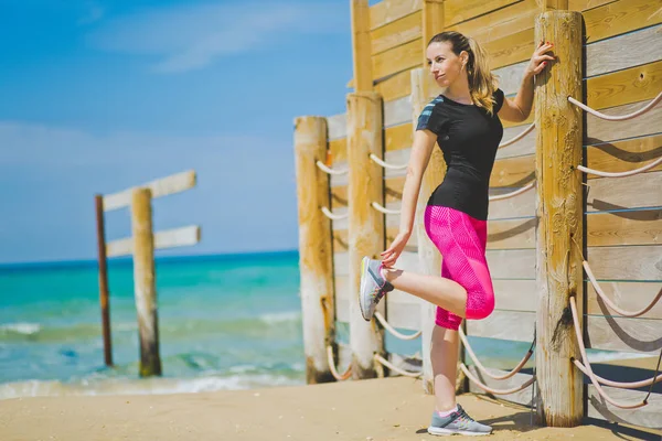 Jonge vrouwen runner poten met longe rekken verlam stretch oefening been strekt. Fitness atlete ontspannen op het strand doen een warming-up vóór haar krachttraining cardiotraining. — Stockfoto