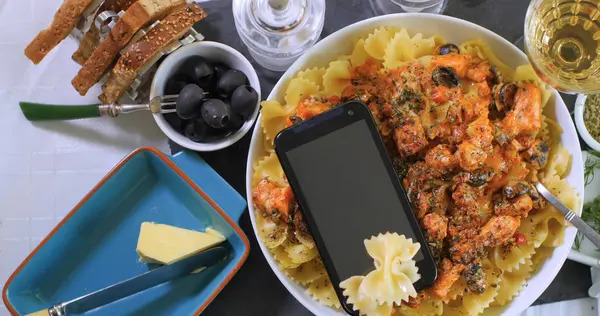 Vista de cerca de arriba hacia abajo de la pasta con salmón fresco, aceitunas negras y smartphone — Foto de Stock