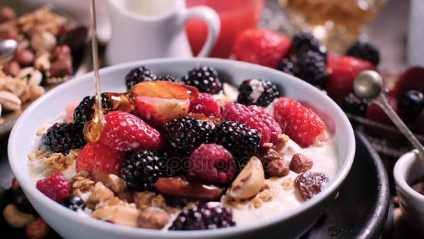 Slow motion view: pouring honey over a bowl of cereals with berries for breakfast with dry fruits — Stock Video