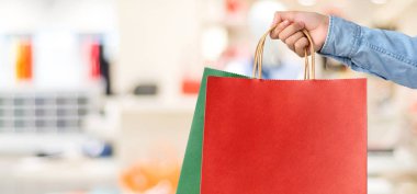 Kırmızı alışveriş çantası bulanıklık mağaza arka planda, banner w tutan el