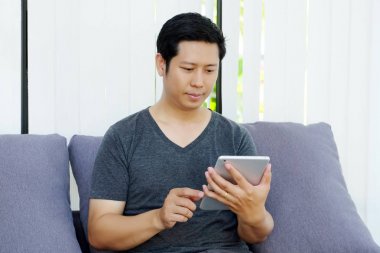 Kanepede oturan ve evde, tablet bilgisayar kullanarak Asya adam lif