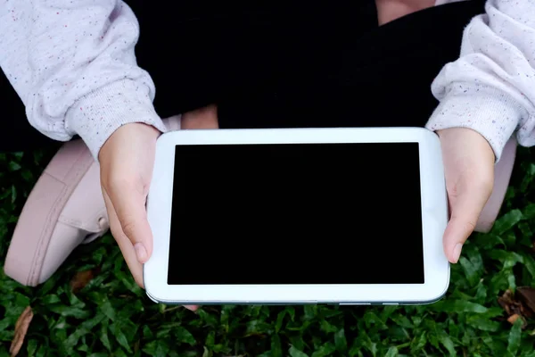 Mano usando la tableta de pantalla en blanco sobre hierba verde fondo — Foto de Stock