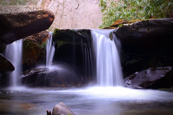 Pequena cachoeira com pedras de rio cobertas de musgo na luz do sol brilhante nas montanhas esfumaçadas — Fotografia de Stock