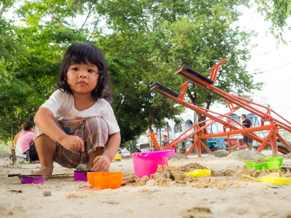 Little Asia girl sitting in the sandbox and playing with toy sand shovel bucket and she was scooping the sand in toy shovel bucket — Stock Photo, Image