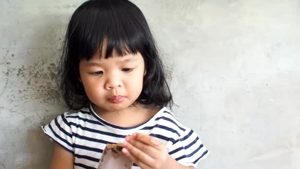 Asijská holčička mají velké oči, stál přední zdi cementu a trochu asijské dívky jí radost jíst čokoládové zmrzliny.