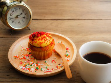 Sarı kek küresel ahşap tabağa koy. Yanında cupcake Vintage çalar saat ve beyaz kahve kupa var. Hepsini tahta masada duruyor.