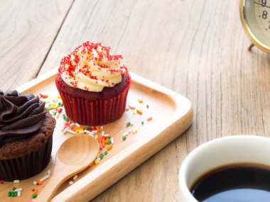 Kırmızı ve çikolata cupcakes küresel ahşap tabağa koy. Yanında cupcake kaktüs ve beyaz kahve kupa var. Hepsini tahta masada duruyor.