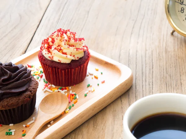 Kırmızı ve çikolata cupcakes küresel ahşap tabağa koy. Yanında cupcake kaktüs ve beyaz kahve kupa var. Hepsini tahta masada duruyor.