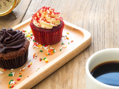 Kırmızı ve çikolata cupcakes küresel ahşap tabağa koy. Yanında cupcake kaktüs ve beyaz kahve kupa var. Hepsini tahta masada duruyor.