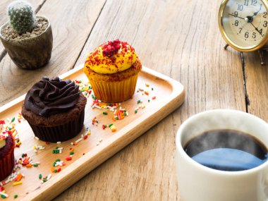 Sarı ve çikolata cupcakes küresel ahşap tabağa koy. Yanında cupcake kaktüs ve beyaz kahve kupa var. Hepsini tahta masada duruyor.