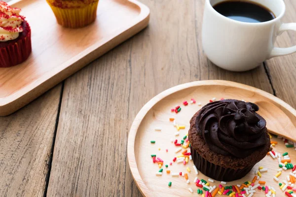 çikolata cupcakes küresel ahşap tabağa koy. Yanında cupcake beyaz kahve kupa var. Arka planda sarı kek ve çikolatalı kek var.