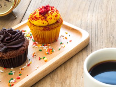 Sarı ve çikolata cupcakes küresel ahşap tabağa koy. Yanında cupcake kaktüs ve beyaz kahve kupa var. Hepsini tahta masada duruyor.