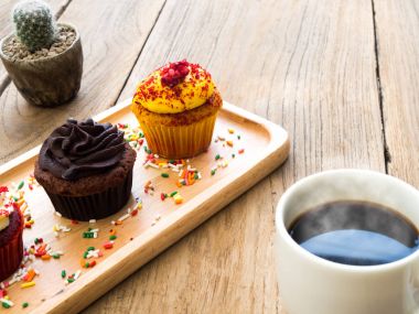 Sarı ve çikolata cupcakes küresel ahşap tabağa koy. Yanında cupcake kaktüs ve beyaz kahve kupa var. Hepsini tahta masada duruyor.