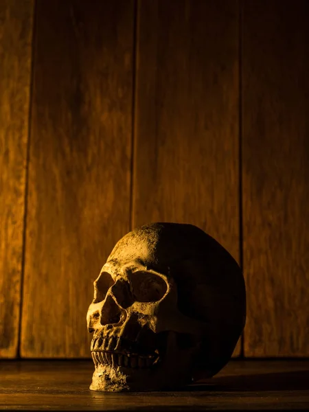 De schedel is geplaatst op een houten tafel. De achtergrond is een houten plaat en het licht van de kaars op de schedel. — Stockfoto