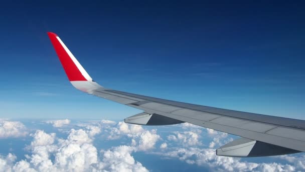 缩小飞在空中的机翼飞机。机翼的尖端是红色的。飞机的顶部是蓝色的天空, 底部是一片白云。从客舱里的旅行者的角度来看. — 图库视频影像