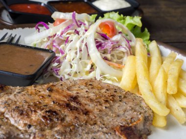 T-bone Steak tuz ve biber, altın kızarmış patates ve yeşil sebzeler ile kapatın. Beyaz tabak, çatal ve bıçak, restoranda ahşap masa