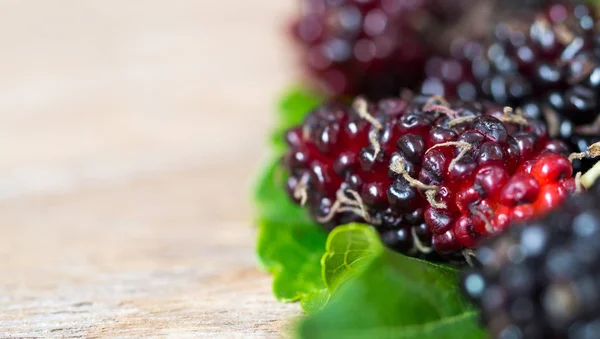 Close up of mulberry with a green leaves on the wooden table. Mulberry this a fruit and can be eaten in have a red and purple color. Mulberry is delicious and sweet nature.