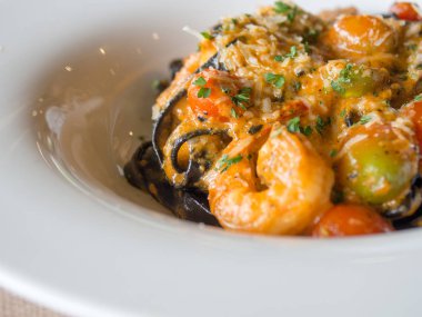 Siyah spagetti domates soslu karides, baharat ve peynir beyaz tabakta domates serpin ile. Taze ve temiz yemekler lezzetli ve nefis görünüyor